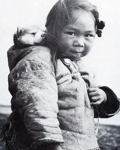 Pequena menina esquimó e seu filhote de cão Husky.