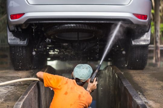 Trabalhador do lava jato pulverizando ao lavar o chassi do carro