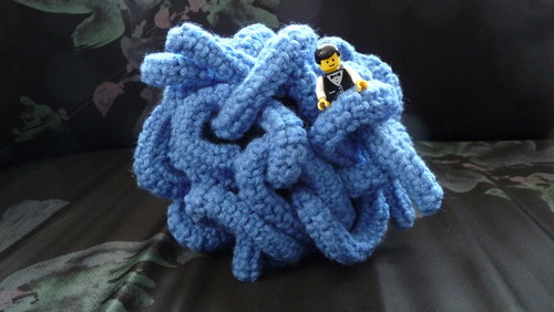 A crocheted version of the pokemon Tangela. This is the back view. a lego man is in the tangles.