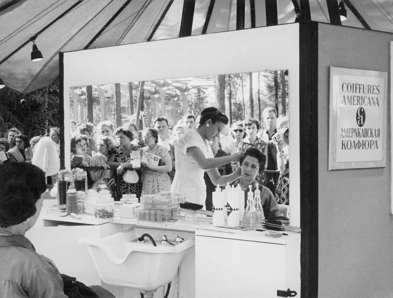 Outdoors hair salon at the USA Expo in Sokolniki Park in Moscow. Photo by Claude Jacoby, 1959. Check out the sign on the right: АмерNканская коафюра. 😅