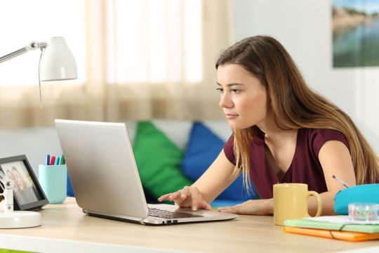 mulher mexe em computador sobre mesa dentro de sua casa durante aulas teóricas online
