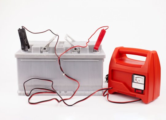 carregador de bateria de carro vermelho com cabos conectados a uma bateria sobre fundo branco