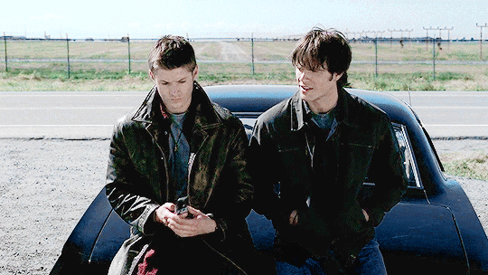 gif of young Dean and extremely young Sam sitting on the hood of the Impala while Dean uses a flip phone