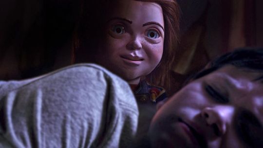 Chucky doll rising from behind a sleeping boy