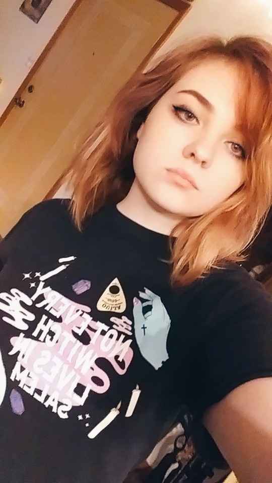 a teenage girl with red hair and on-point eyeliner, with a witchy T-shirt that reads 