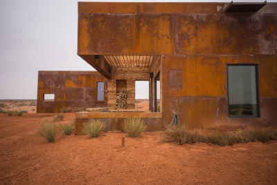 archatlas:<br /><br />Mexican Water Cabins DesignBuildBLUFF<br /><br /><br />The Mexican Water Chapter of the Navajo Nation partnered with Design Build BLUFF (and University of Colorado Students)  to construct two rentable cabins; with the idea that tourism dollars otherwise lost outside the boundaries of the reservation could rather stay and help encourage the local economy. Influenced by the landscape and distant views of the Blue Mountains and Monument Valley, the design led to the development of two “sibling” cubes. One rests on the landscape while the other emerges from it. <br /><br /><br />Images and text via DesignBuildBLUFF<br /><br /><br />