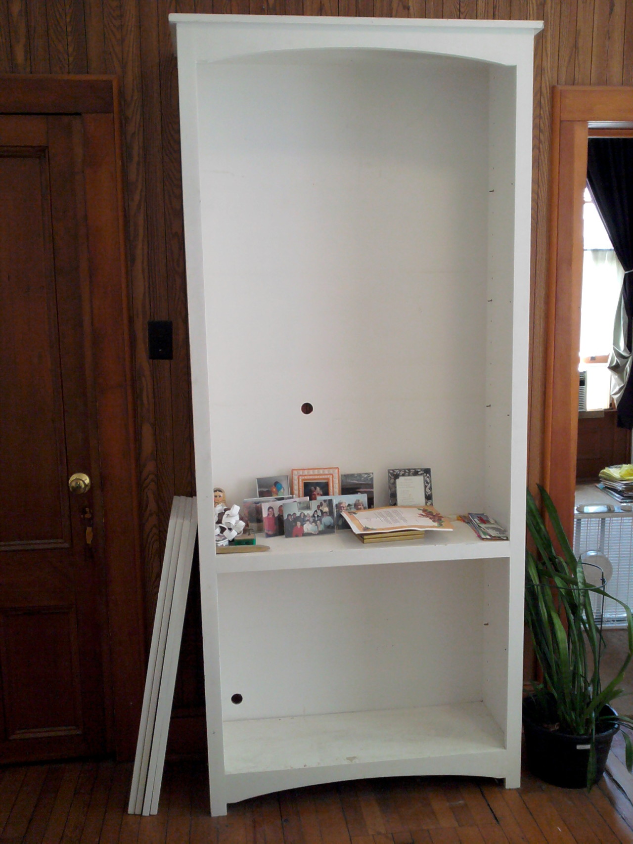 tall white bookcase with a small collection of junk on its one remaining shelf