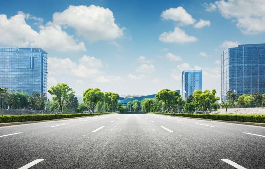 imagem mostra uma rua pavimentada sem pessoas e sem carros com predios ao redor e o ceu azul acima