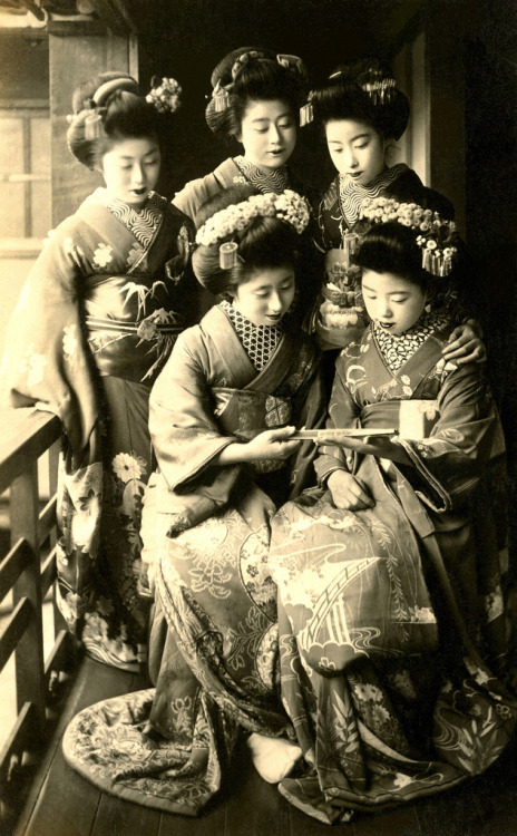Podziwianie składanego wentylatora z lat 1910 (autor: Blue Ruin1) „Momotaro, siedzący po lewej stronie, oraz czterech innych Maiko (Apprentice Geisha), podziwiających dekoracje na składanym wachlarzu.  Archiwalna pocztówka z przełomu lat 1910 lub 20.  ”