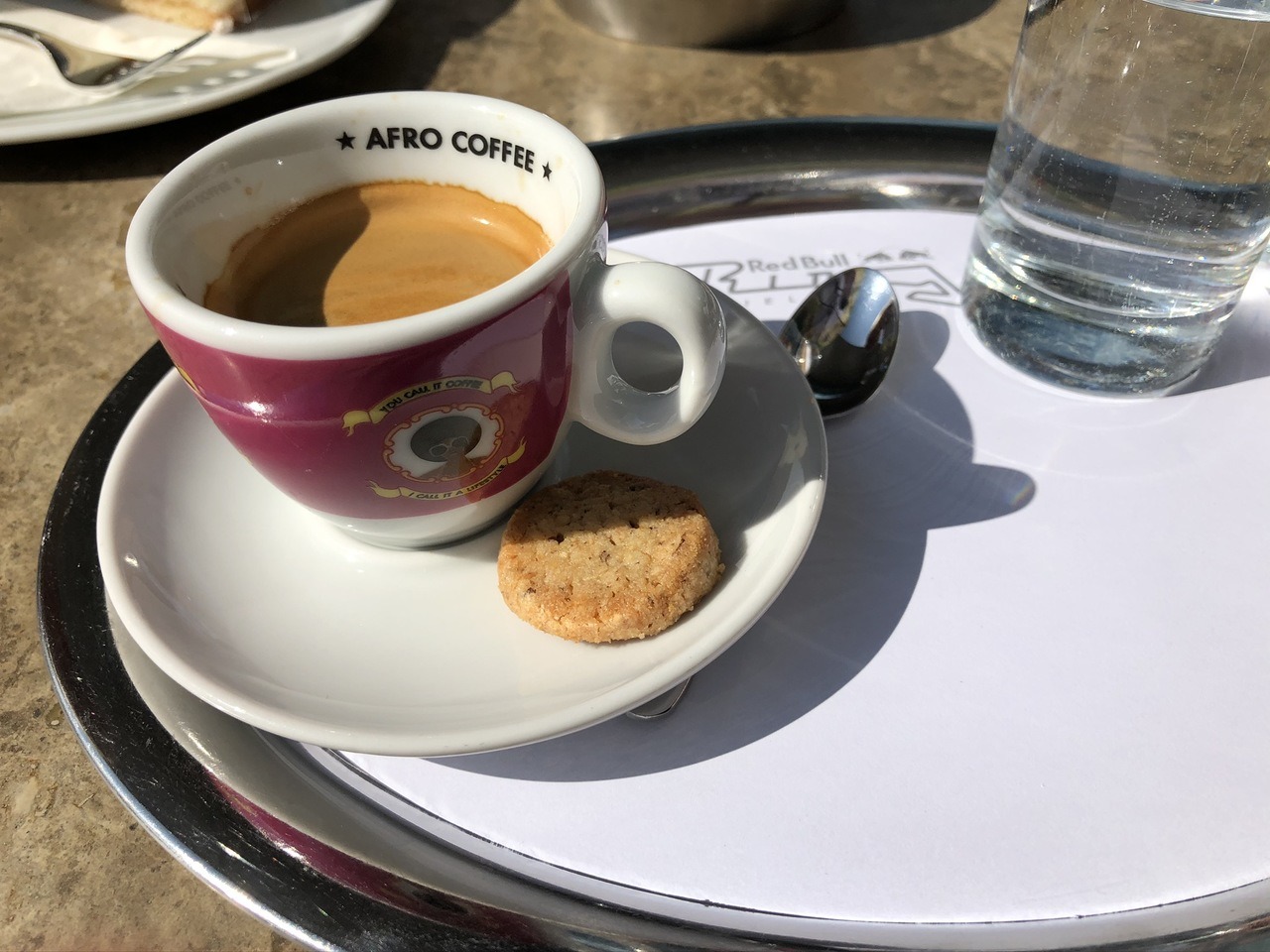 Afro Coffee Espresso mit kleinem Keks und einem Glas Wasser.
