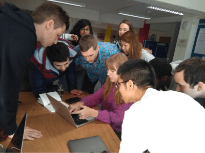 Ten developers huddled around a laptop using mob programming to solve a problem together.