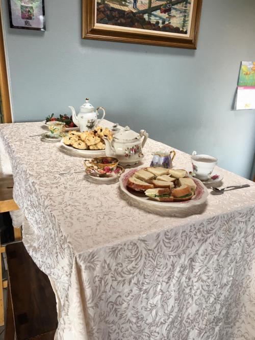 A picture of a table with several plates of things: little sandwiches, scones, strawberries, teacups