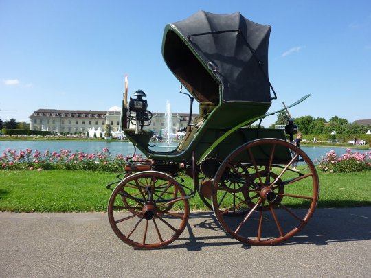 1888 flocken elektrowagen tido como o primeiro carro eletrico do mundo e exposto em uma pista com plantas e flores ao fundo