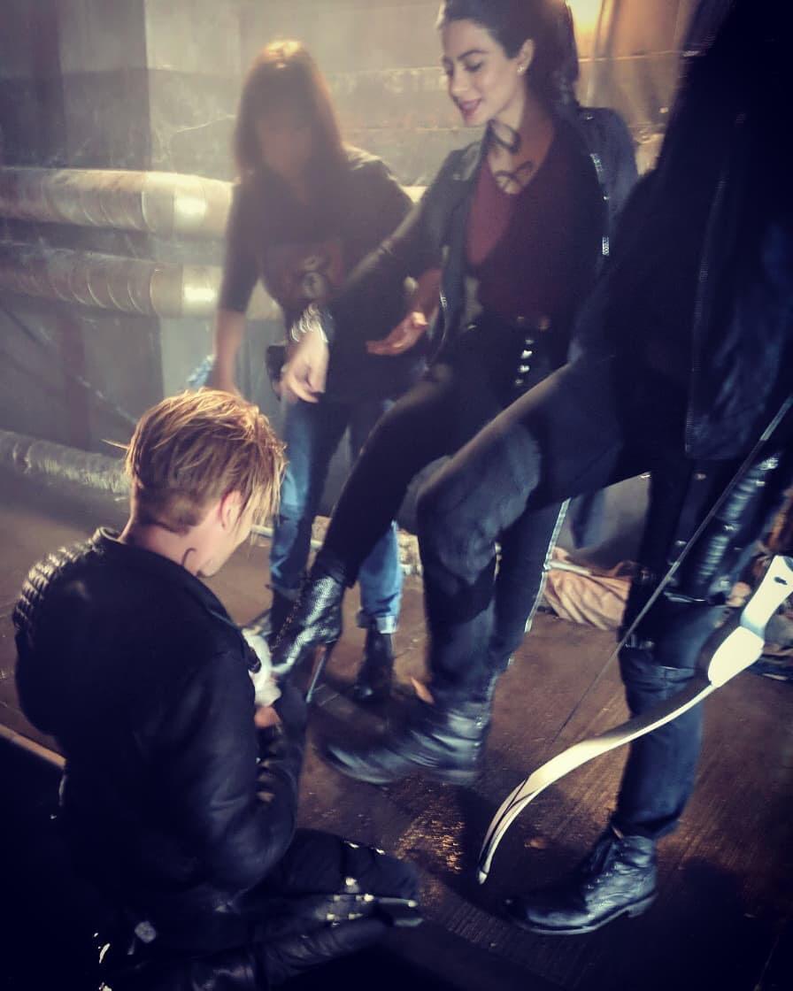 Dom kneeling, cleaning Eme's and Matt's shoes. All three are in costume.