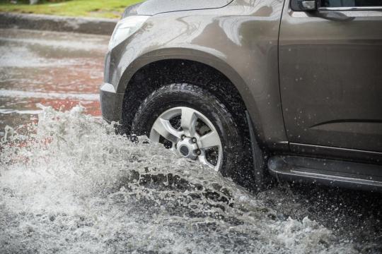 carro passando por um trecho alagado do asfalto com a água quase na metade de sua roda