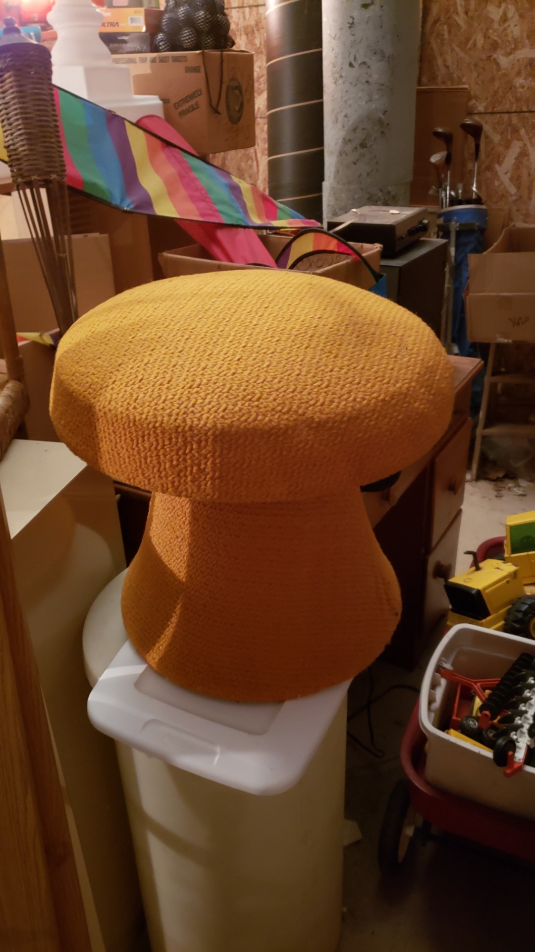 A golden ottoman shaped like a toadstool sitting on top of lots of other stored items.