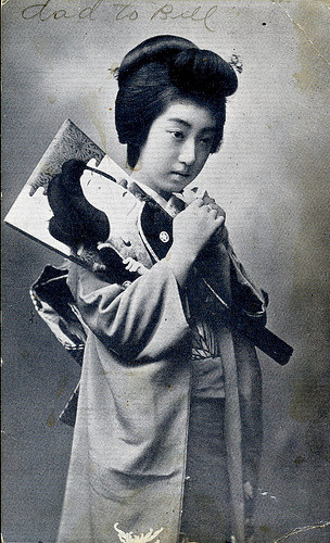 Geisha Teruha z wiosłem Hagoita (1920) Pocztówka przedstawiająca gejszę Teruhę z wiosłem Hagoita używaną do grania w noworoczną grę Hanetsuki, podobną do Badmington. (Źródło)