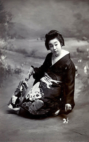 Geiko Kingo (1905) Kingo a Geiko (Geisha) z Osaki.  Tutaj trzyma wiosło Hagoita i sięga po lotkę, aby zagrać w noworoczną grę Hanetsuki. (Źródło)