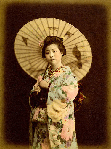 Falcon and Sparrow Wagasa (1890)
“ A Hangyoku (Young Geisha) dressed in a fabulous kimono covered in hand-painted tree peonies, holding a Wagasa (paper umbrella) decorated with a Falcon in a tree and Sparrows in flight. The decoration on her Wagasa...