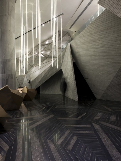 inthenoosphere:<br /><br />Taking inspiration from the surrounding mountain range in Nanshan, the newly designed Chongqing Mountain  City Sales Office has come to life. The interior architecture of the office, designed by One Plus Partnership, has its valleys and its peaks. The space is fitted with an abstract version of a mountain, by connecting triangular grey marble faces to one another. The “mountain range” is central in the office, and custom built angular bronze desks are randomly scattered around architectural element. A field of tube lighting drapes down from the ceilings creating an aesthetic of a rain shower pounding down on the rocks.(via KNSTRCT)<br />