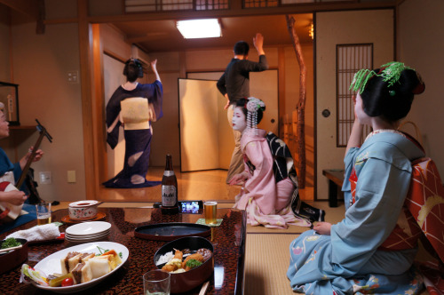 At a ozashiki: Geiko Yasuha playing Yakyuken with a guest, while jikata geiko Satokazu plays the shamisen. Maiko Satoharu and Miena watch.