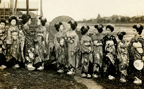 Maiko Momotaro and Friends on the Riverbank (1920) „„ Grupa Maiko (Apprentice Geisha) stojąca na brzegu rzeki.  Maiko Momotaro jest trzeci z lewej strony, ma Maiko Fumiryu.  Ta pocztówka pochodzi z późnych lat 1910 lub wczesnych lat 20. XX wieku. ”(Źródło)”